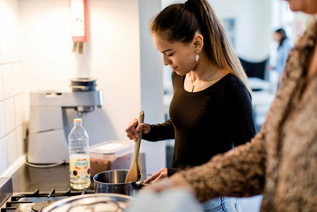 Ung tenåringsjente er sammen med en voksen og rører i en gryte i et privat fosterhjem.
