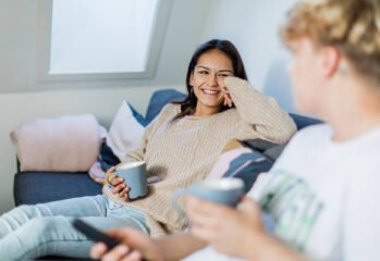 To unge prater sammen i en sofa med en kopp i hånden.