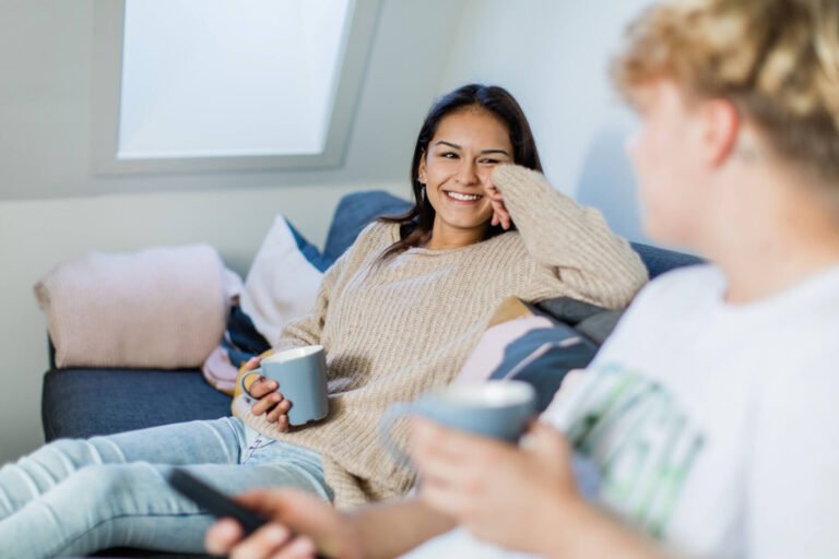 To unge prater sammen i en sofa med en kopp i hånden.