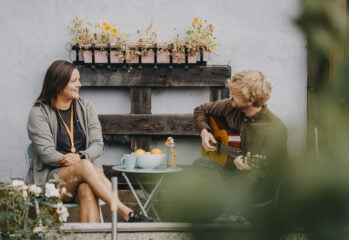 Kvinne og mann som spiller gitar ved bord i hage