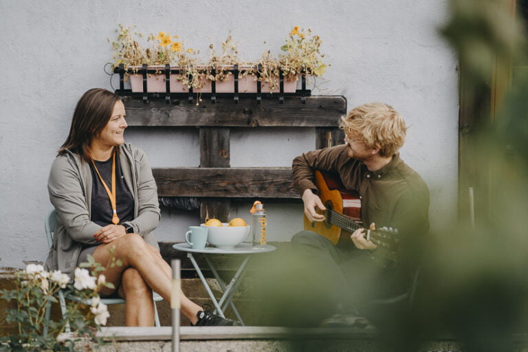 Kvinne og mann som spiller gitar ved bord i hage