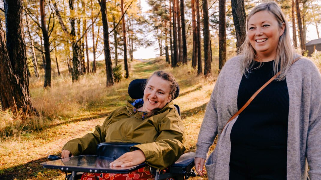 Kvinne i rullestol på tur i skogen med sin kvinnelige BPA-assistent
