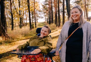 Kvinne i rullestol på tur i skogen med sin kvinnelige BPA-assistent