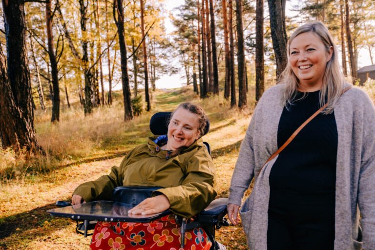 Kvinne i rullestol på tur i skogen med sin kvinnelige BPA-assistent