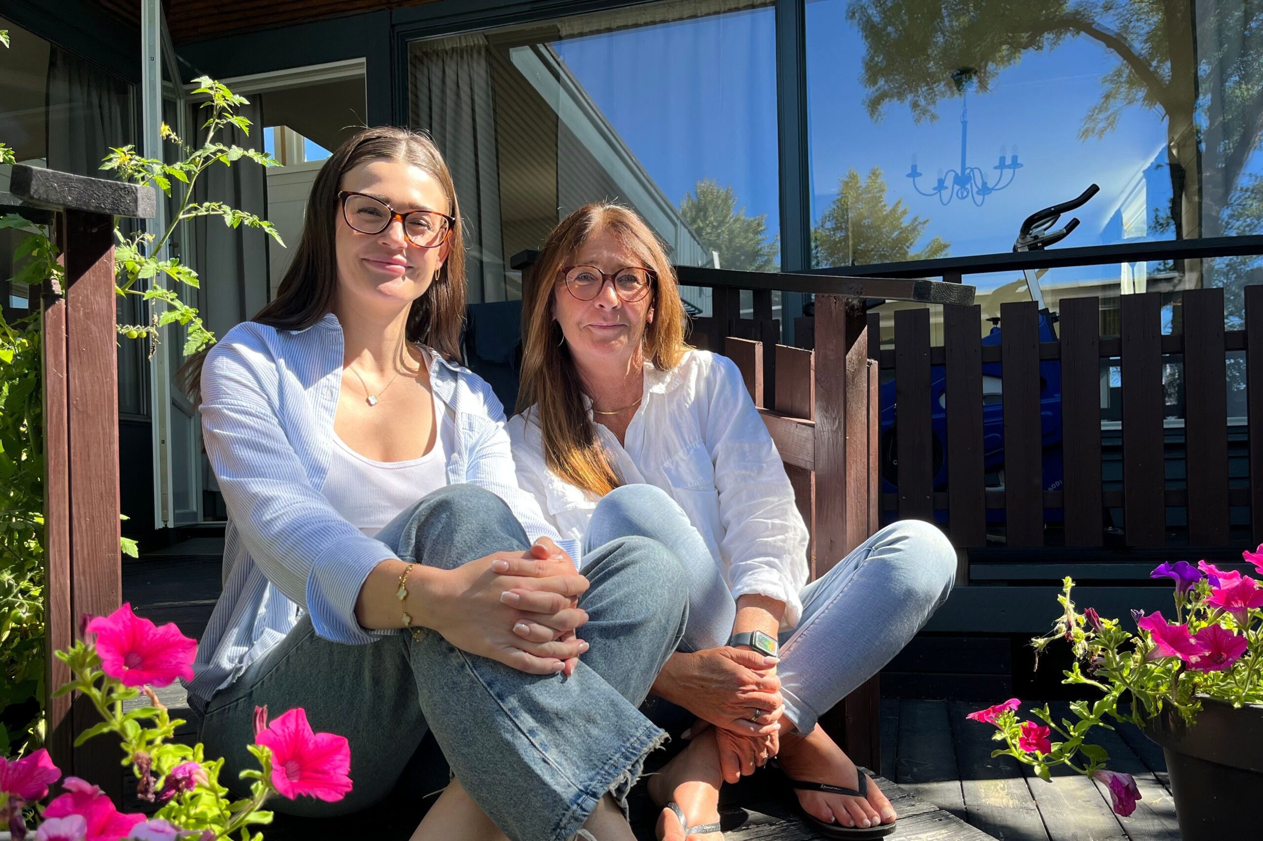 To kvinner sitter på en solfylt terrasse omgitt av blomster