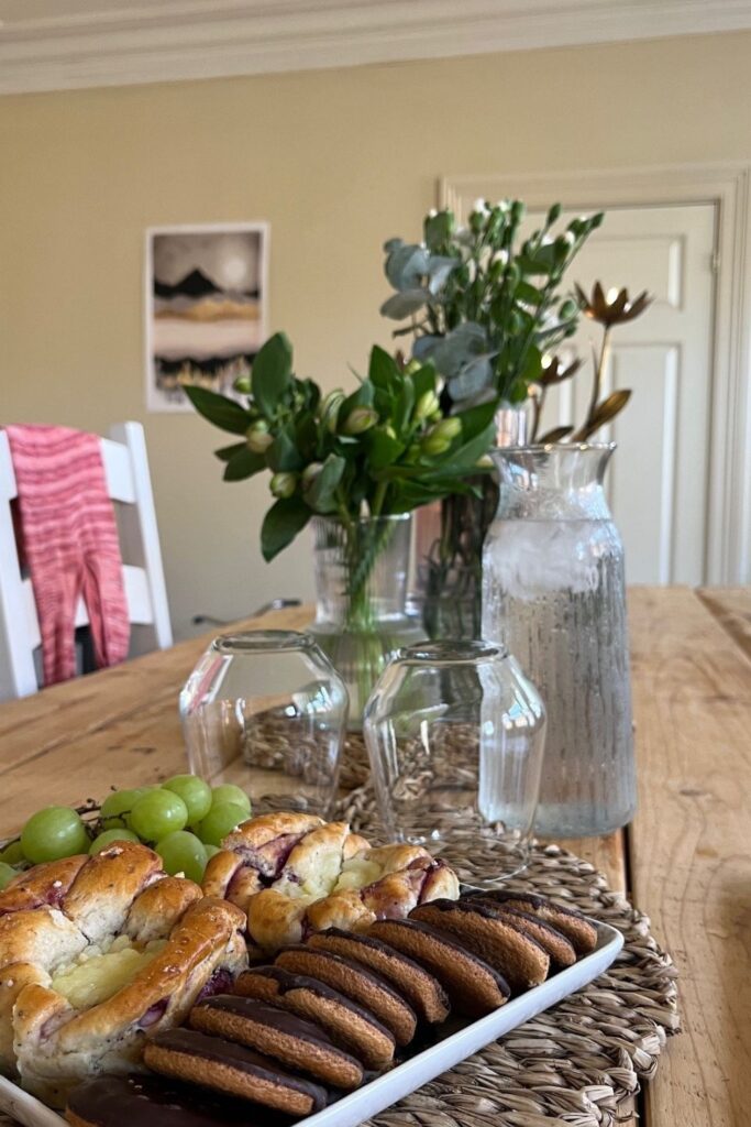 Isvann i karaffel og kjeks og boller på fat på et langbord dekorert med blomster i vase.