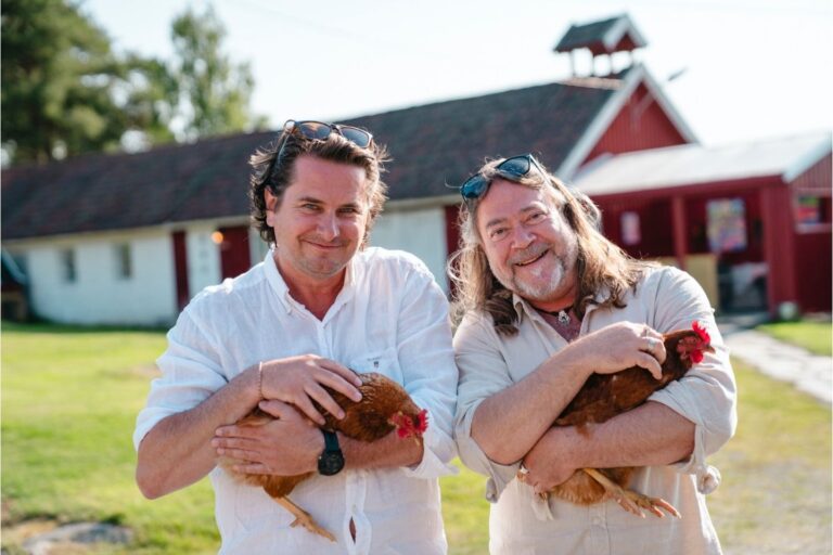 To menn bærer hver sin høne foran en gård