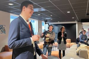 Høy ung mann står ved talerstolen. Kameramann i bakgrunnen.