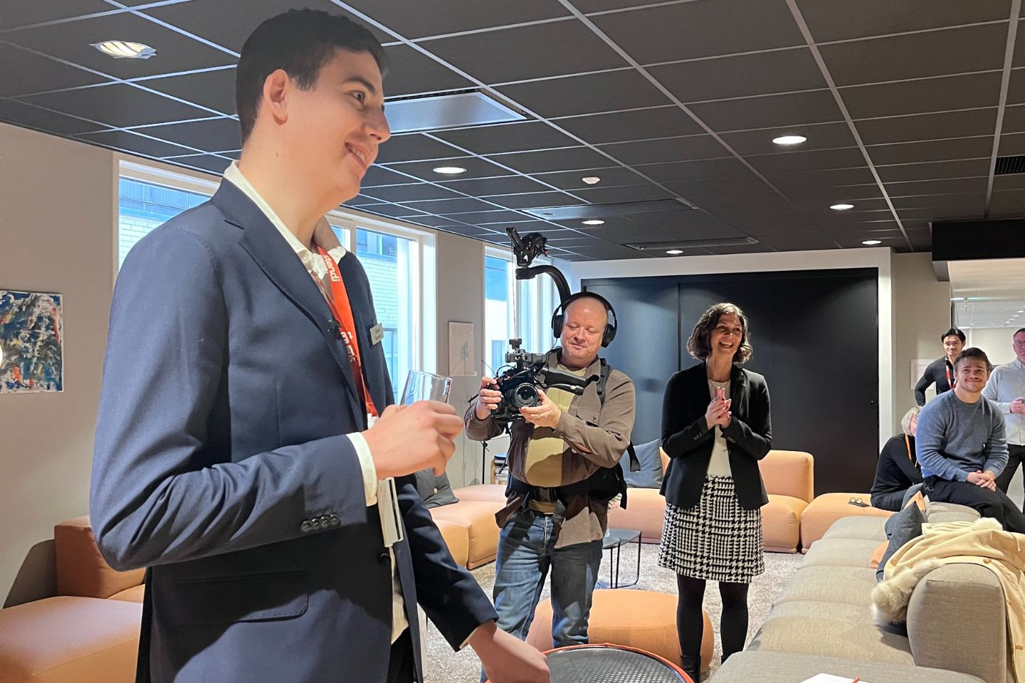 Høy ung mann står ved talerstolen. Kameramann i bakgrunnen.