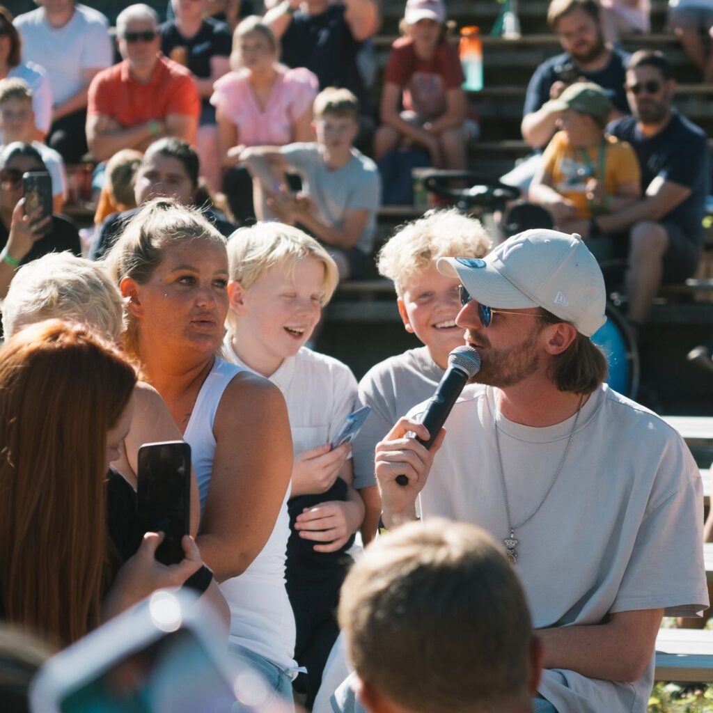 Tix sitter blant barn i publikum med en mikrofon